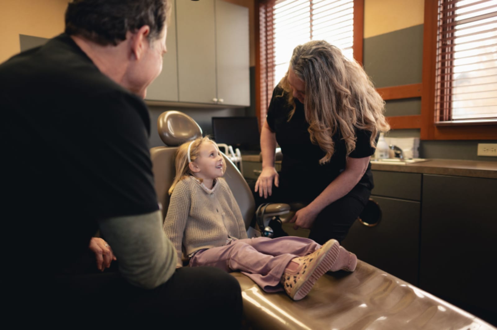 Dental professional performing a procedure on a child with parents present in the operatory