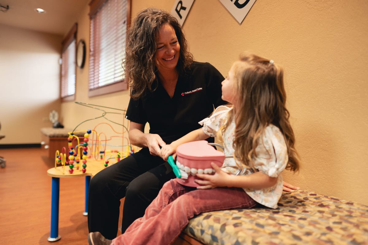 Female dentist discussing oral care with young patient in dental office treatment room.