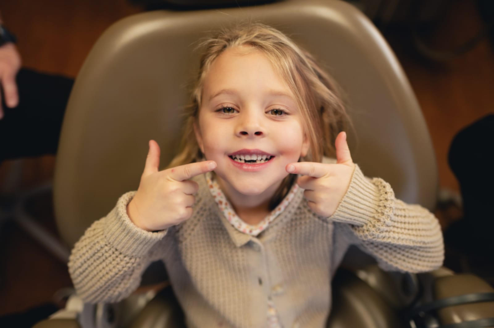 Young girl sitting in dental chair giving thumbs up with a big smile