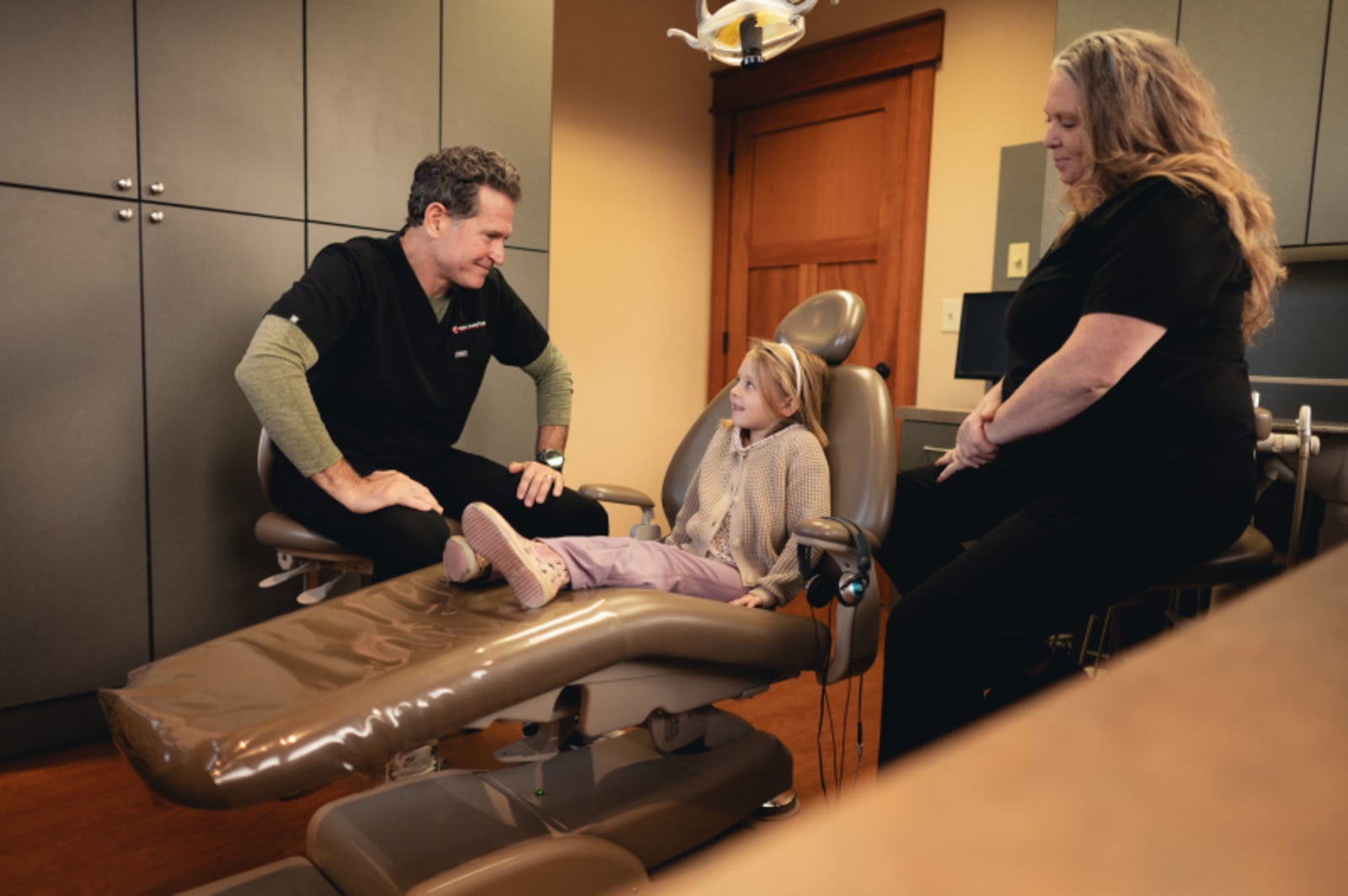 Pediatric dental professional demonstrating airway evaluation technique on a model with patients observing in treatment room.