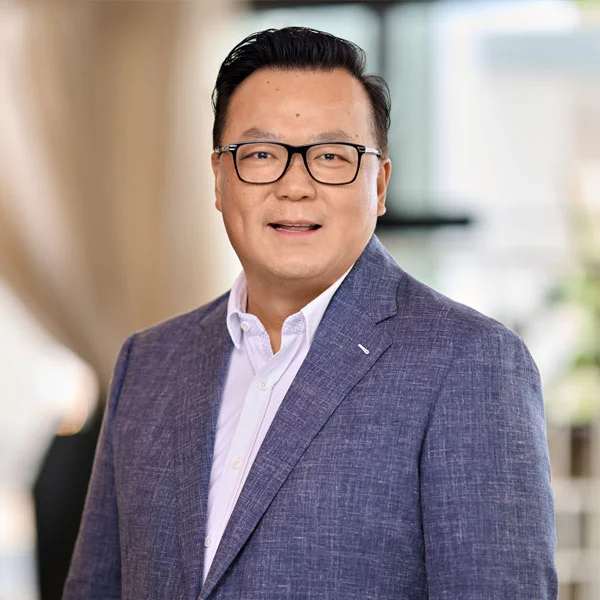 Portrait of a man wearing glasses and a blue blazer over a white shirt, smiling in a bright indoor setting.