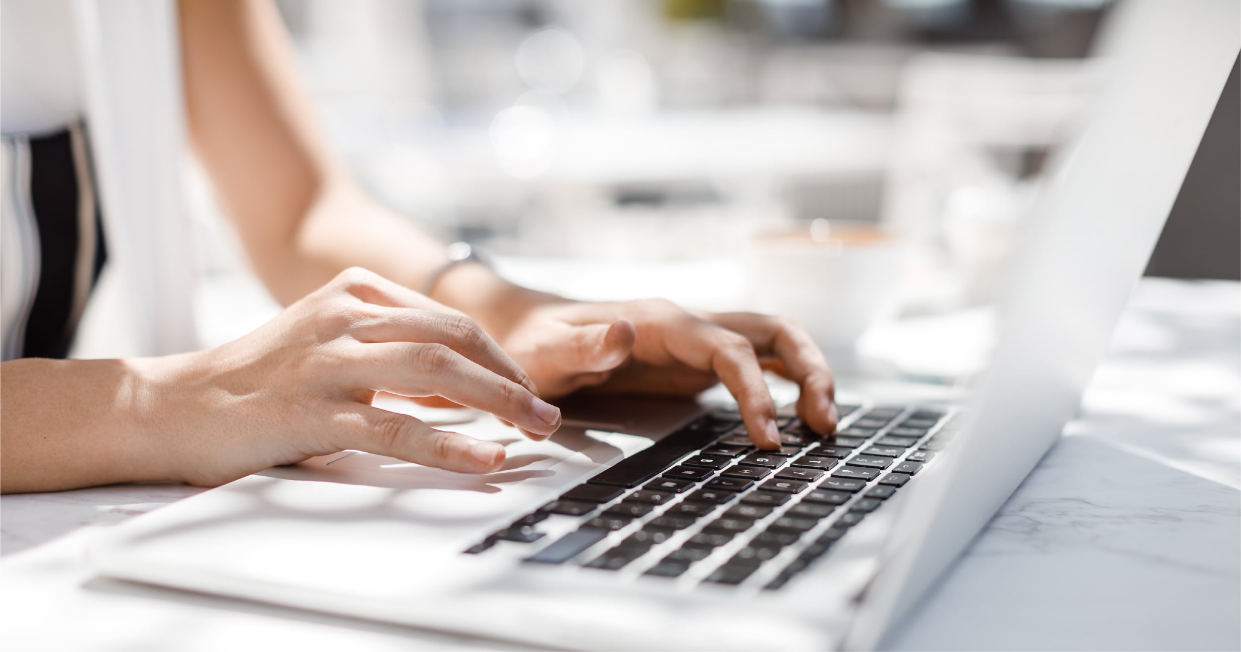 Close-up of hands typing on a laptop keyboard on a white marble table outdoors.