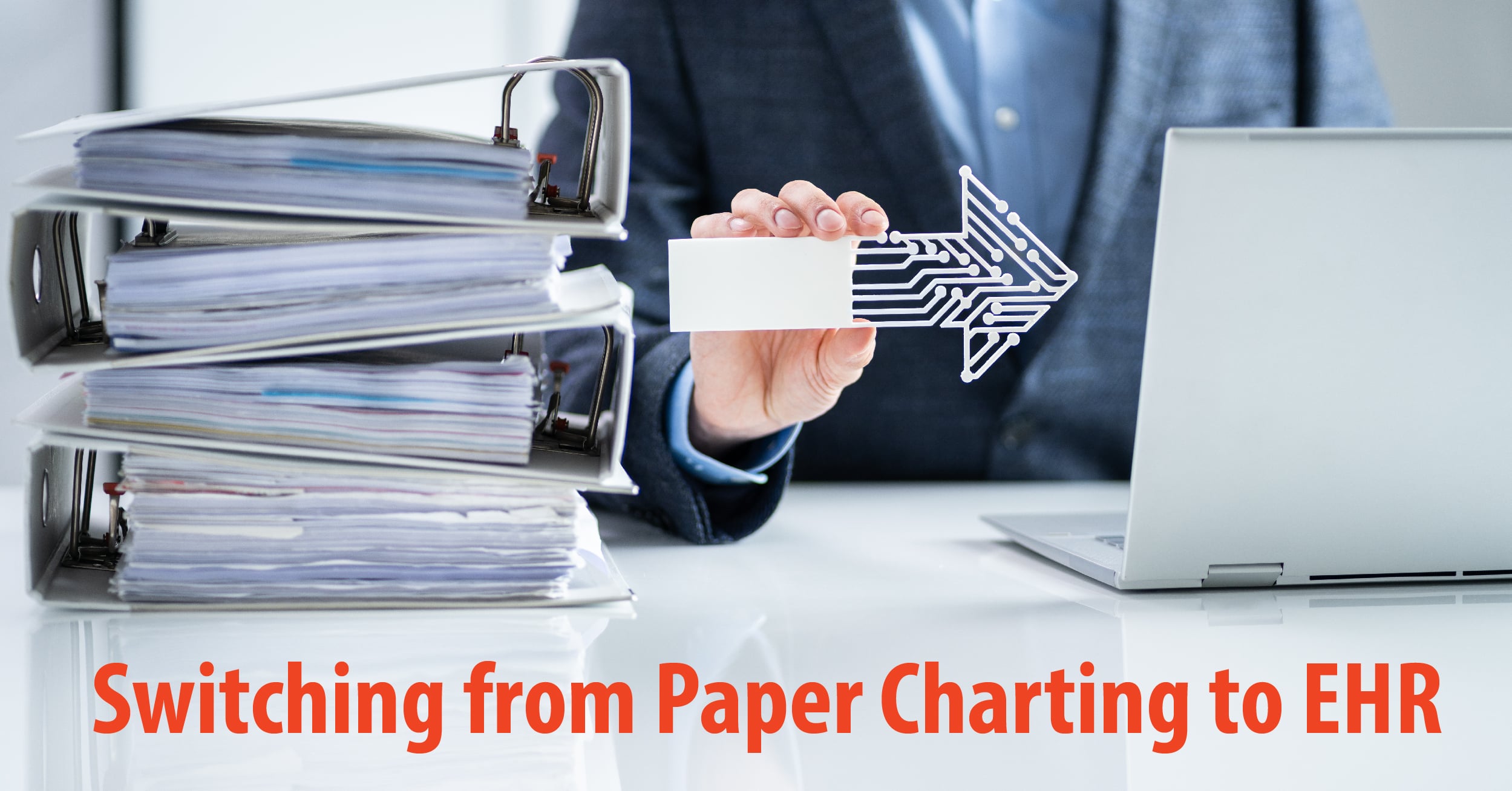 Hand holding an arrow pointing right between stacks of paperwork and a laptop representing switch from paper to EHR.