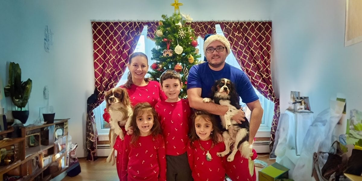 Family of two adults and three children in red pajamas posing with two dogs in front of a Christmas tree.