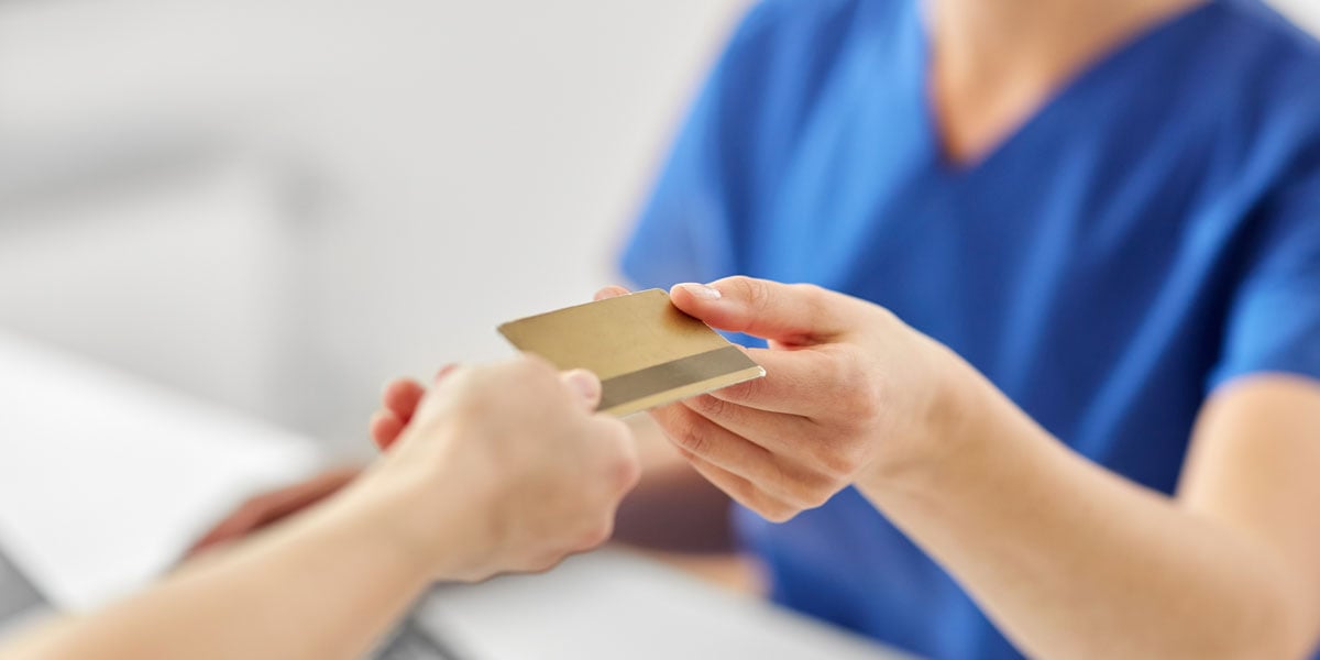 Close-up of two people exchanging a credit card, one wearing blue scrubs in a clinical setting.