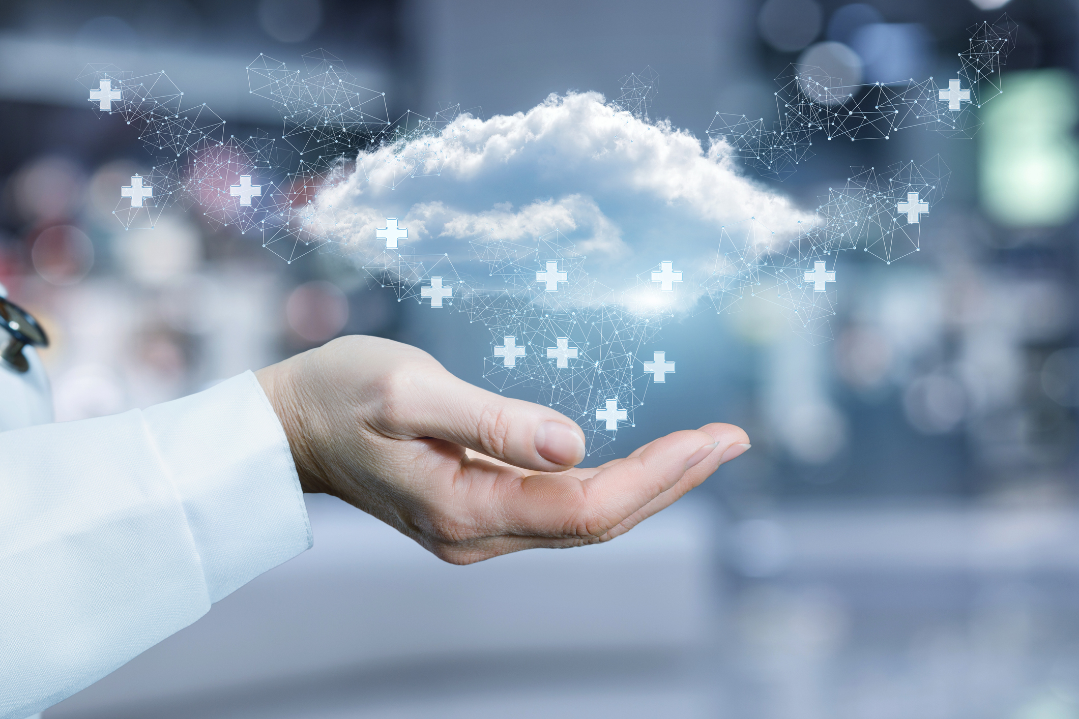 Hand of a medical professional holding a cloud with digital health cross symbols floating above it.