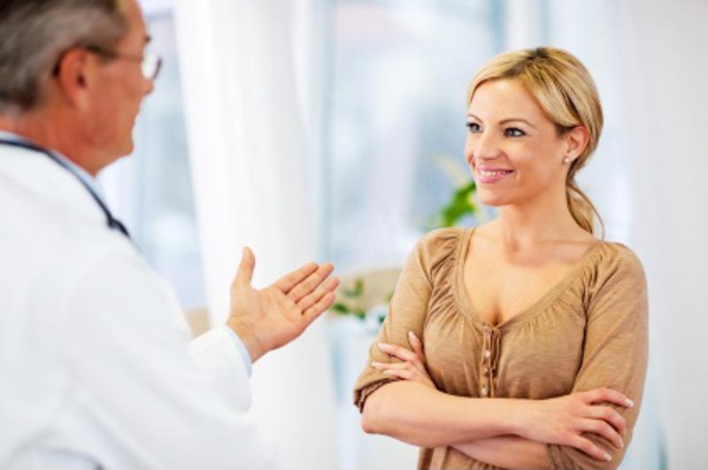Smiling woman with arms crossed listening to a doctor who is gesturing while talking.