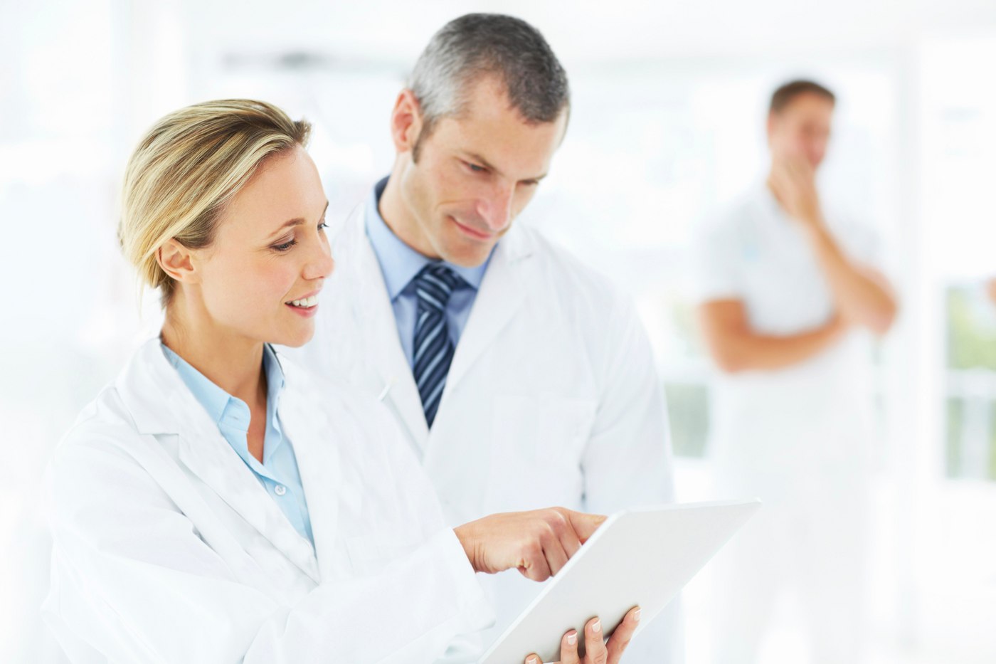 Female doctor showing male doctor information on a tablet, another doctor blurred in background.