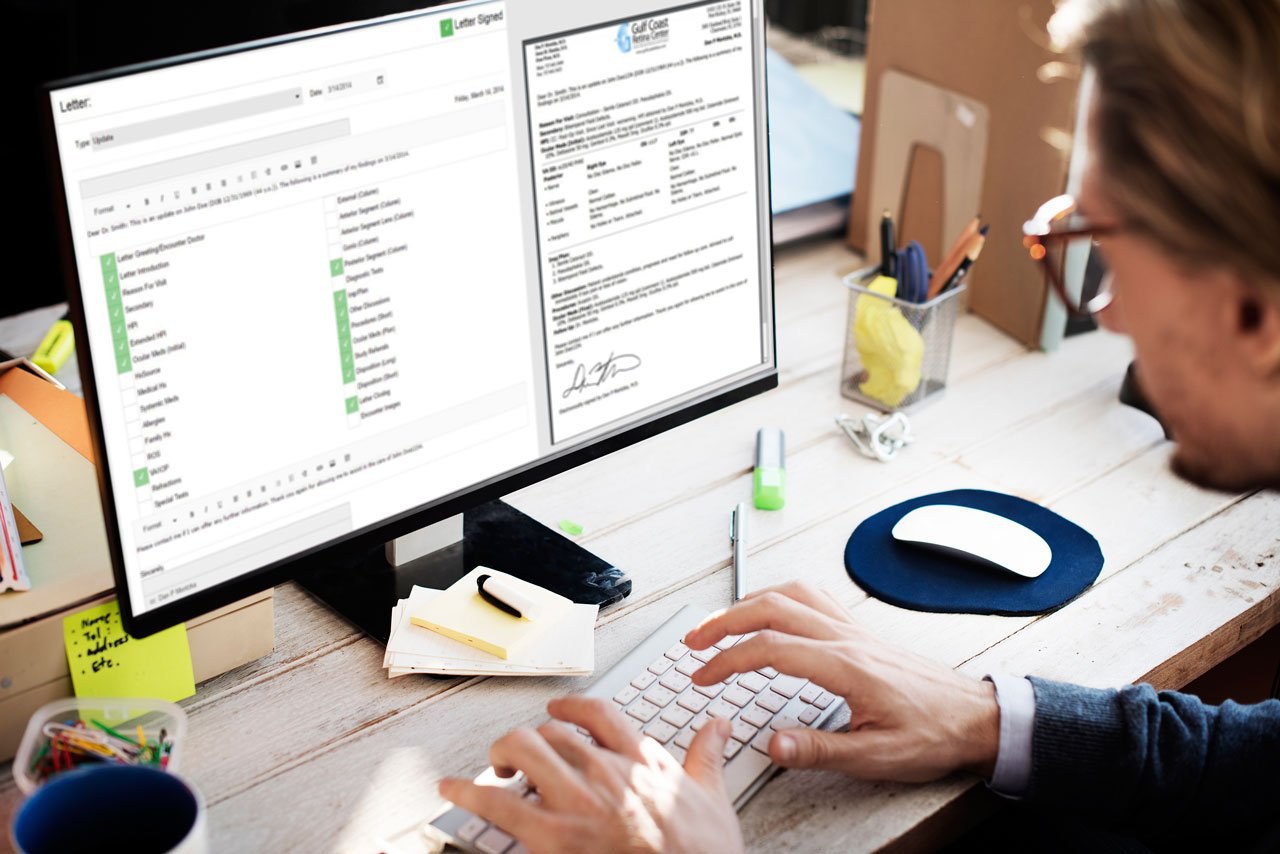 Man typing on keyboard at desk with dual-monitor display showing a document and checklist.