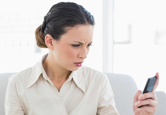 Woman with braided hair looks confused or frustrated while holding a smartphone in her hand.