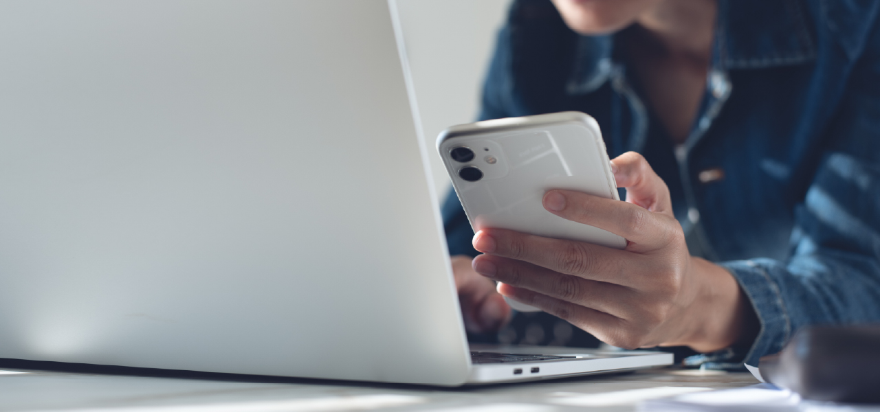 Person holding smartphone in one hand while using a laptop with the other hand.