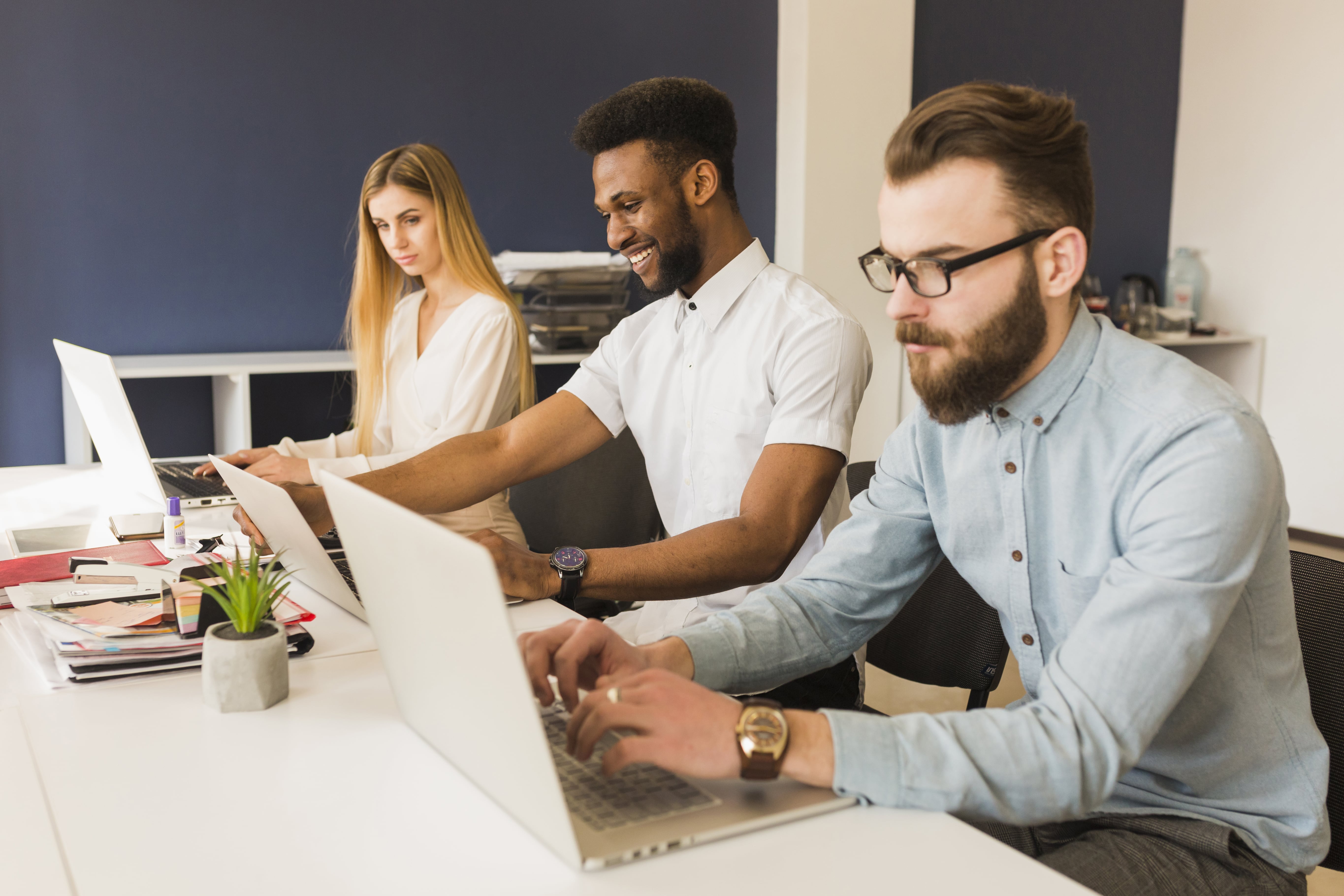 Office workers seated at a large desk working on laptops
