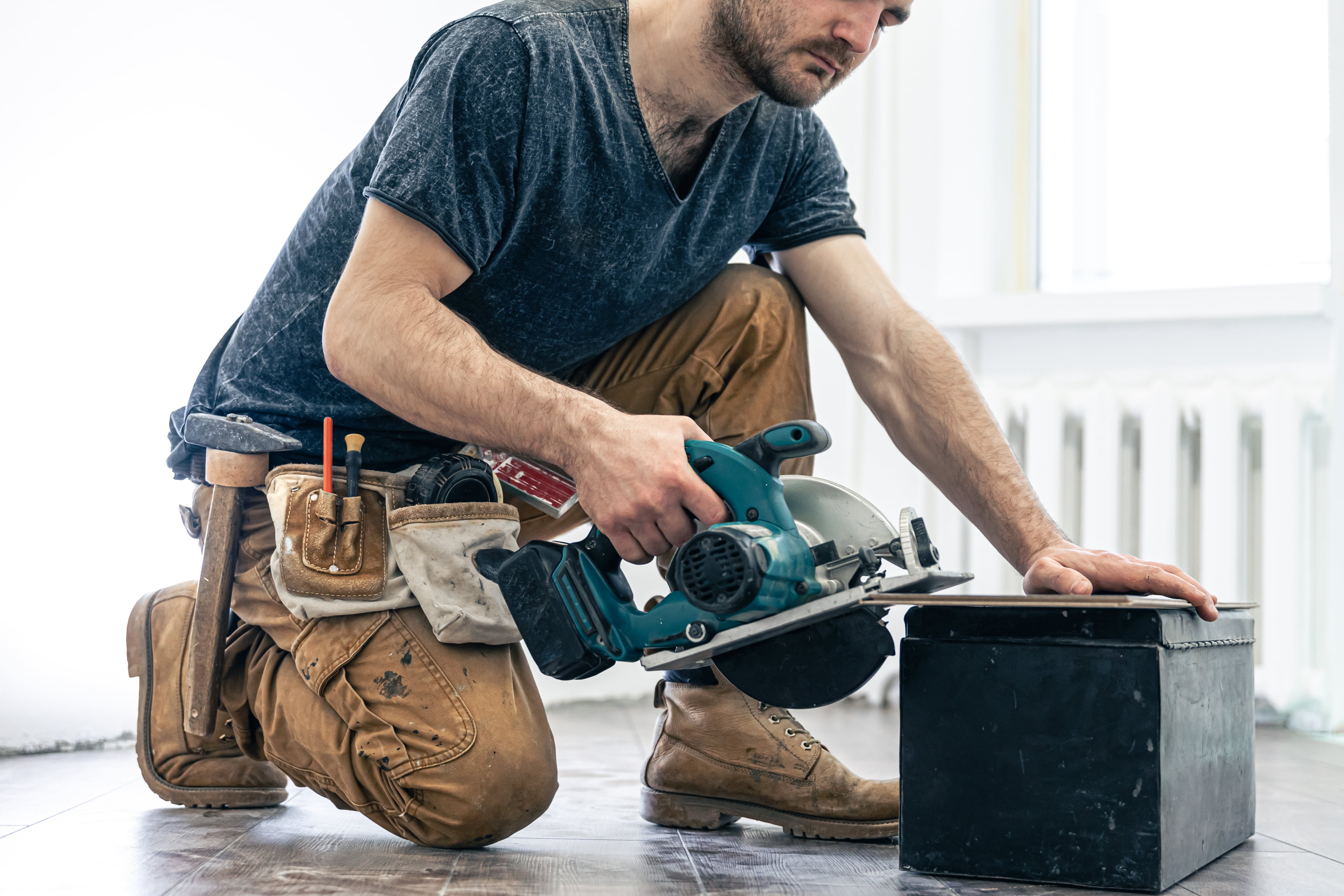 Carpenter kneeled over using circular saw
