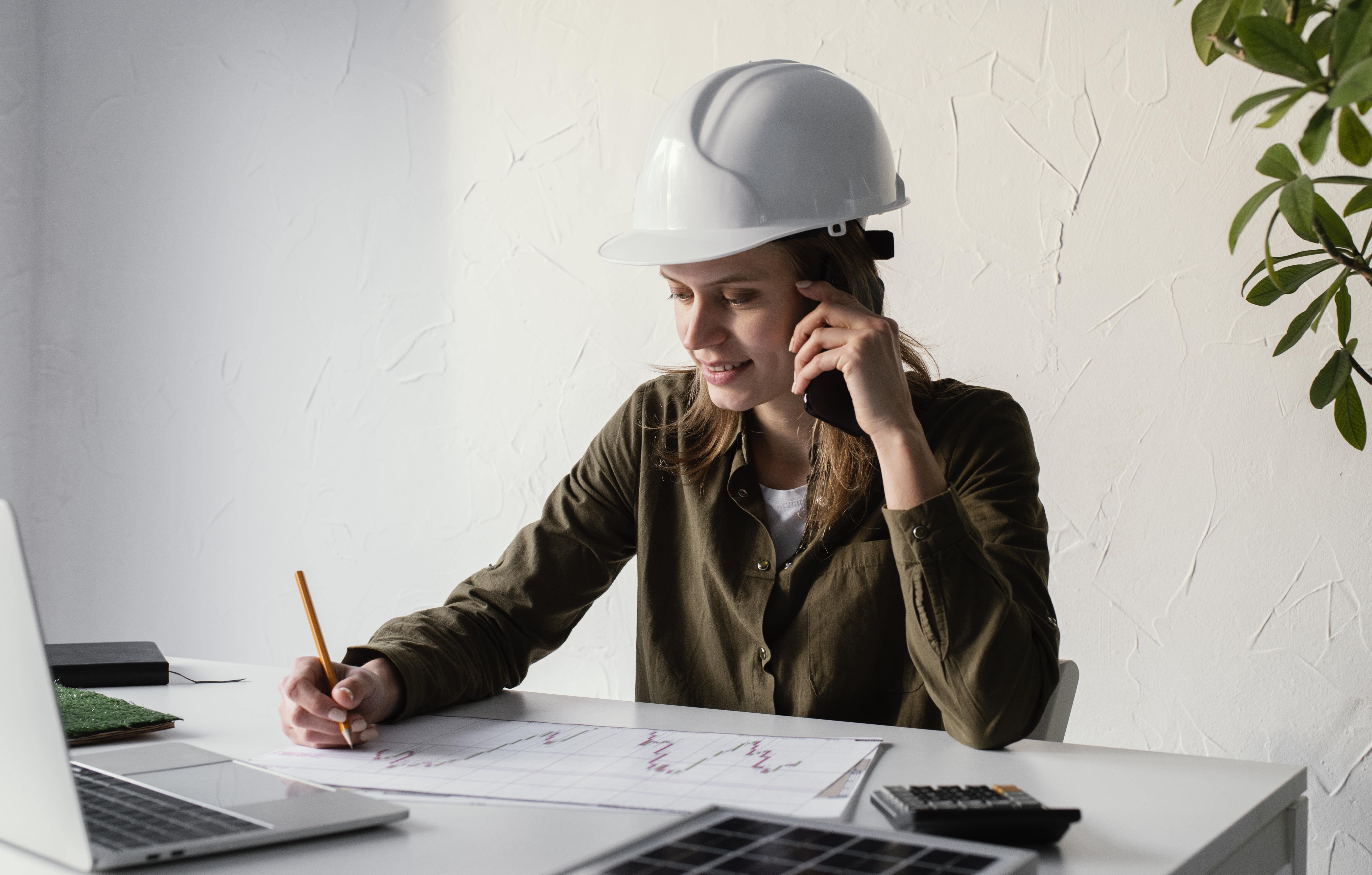 Female engineer speaking on phone while taking notes at desk