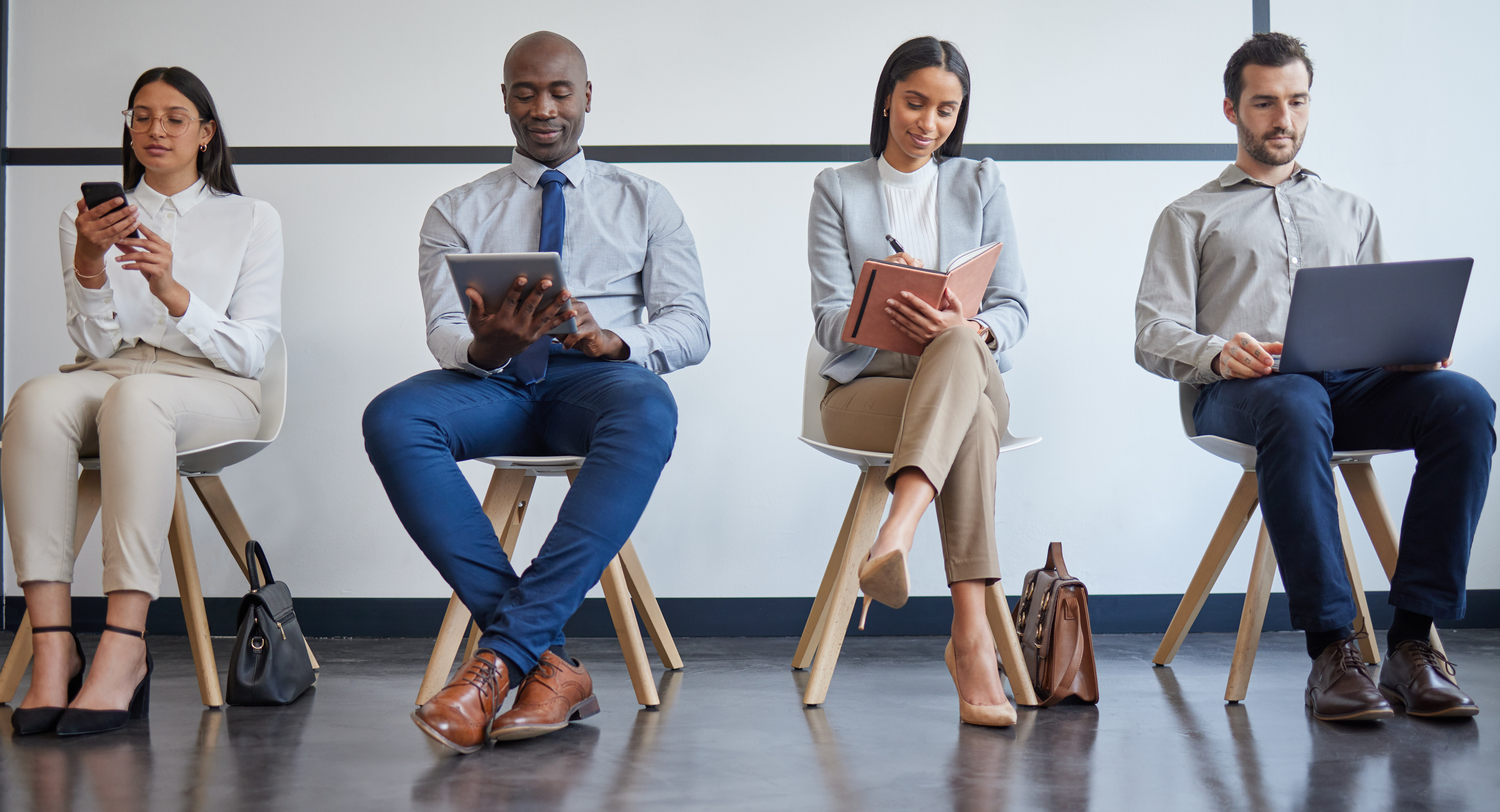 Seated office workers in chairs taking notes on either a mobile phone, tablet, notebook or laptop.