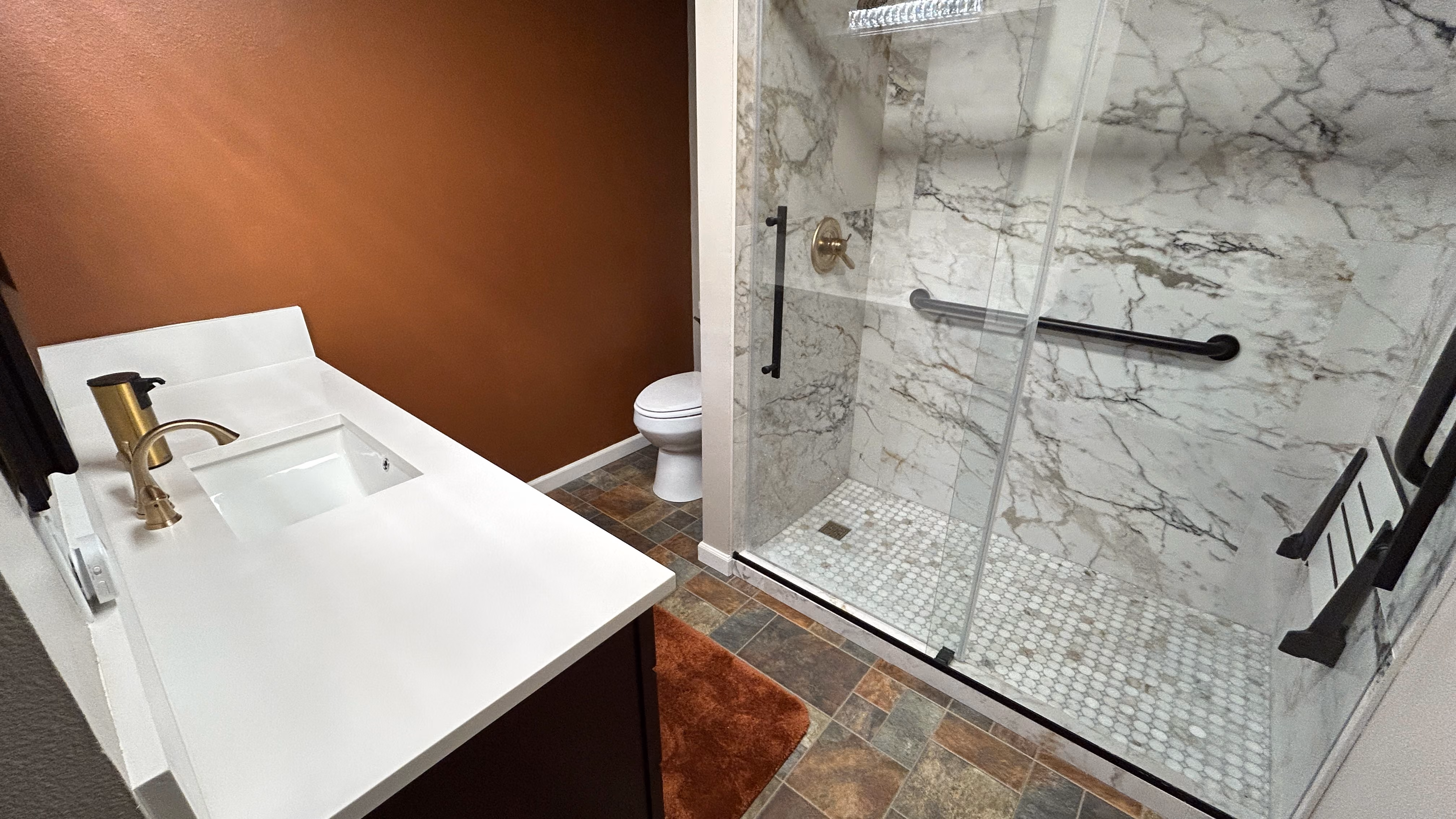 A bathroom remodel in Canby, Oregon featuring a new quartz countertop, sink and faucet installation and a new tile walk in shower with glass doors, grab bars, and a shower bench installation.