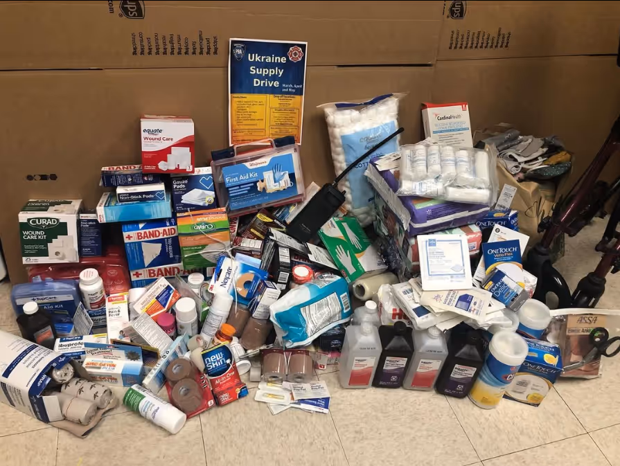 A pile of various medicine bottles and containers made of plastic, alongside other items, positioned on the floor. The scene is indoors, featuring packaging and labeling details visible on the cartons and boxes.


