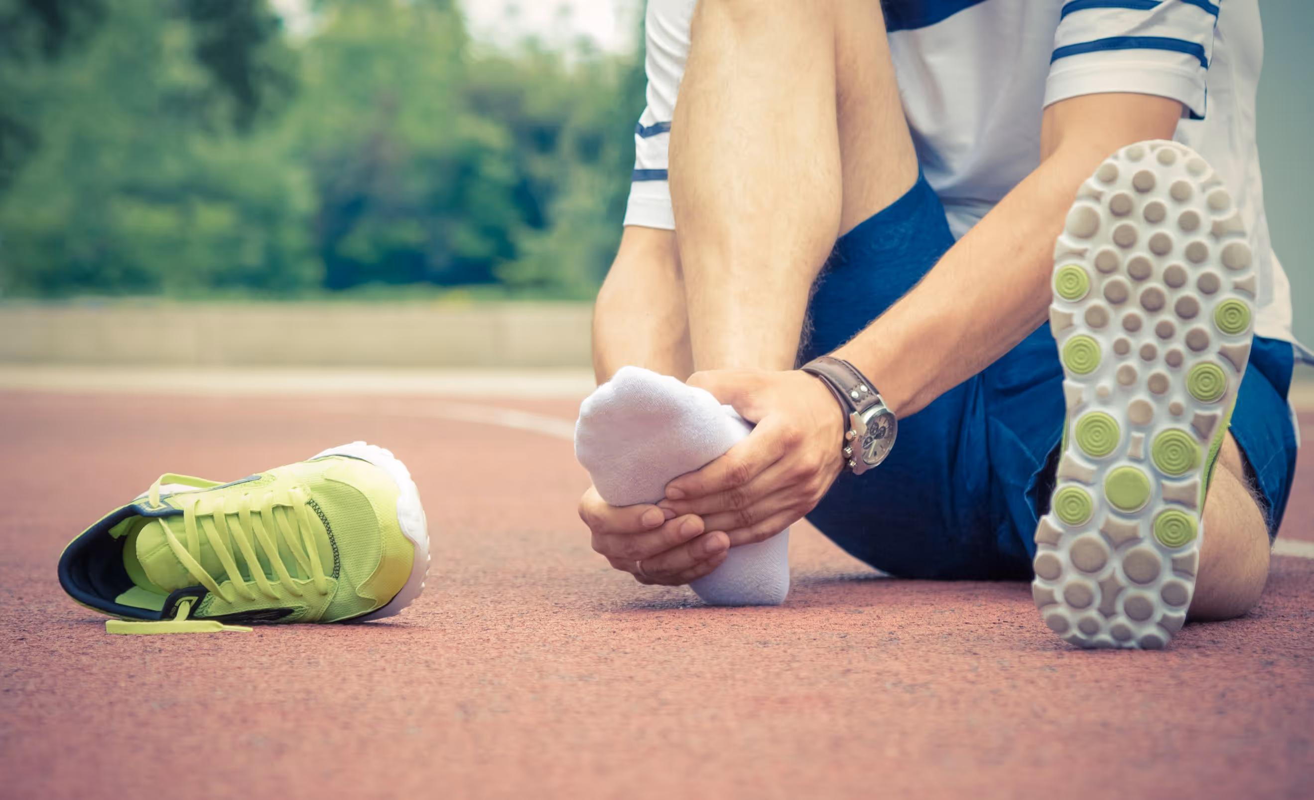 Man in Los Angeles sitting on ground tying shoes, inner ankle swelling, arch pain from flat feet.
