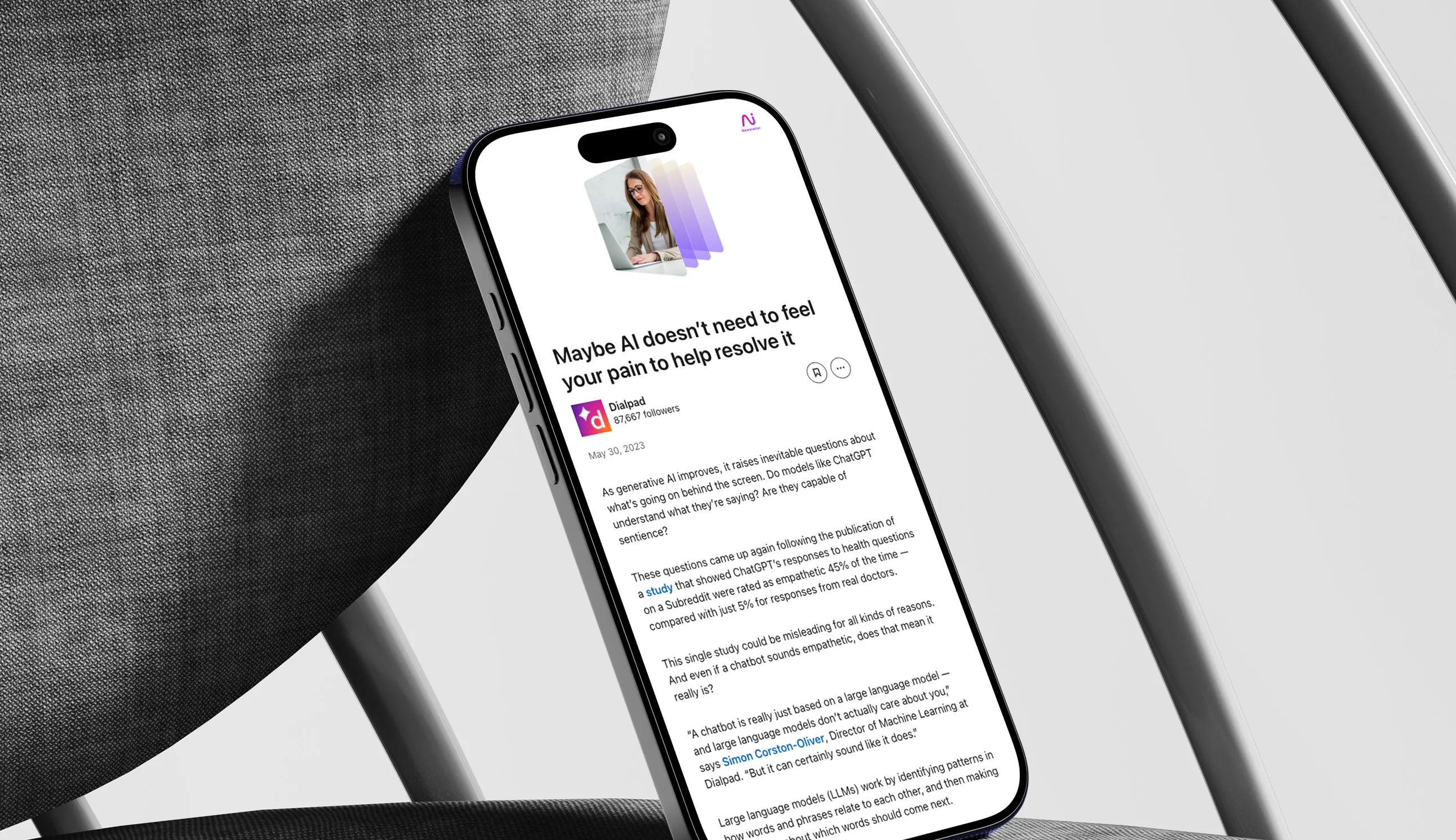 Smartphone on a gray chair screen showing an article titled 'Maybe AI doesn't need to feel your pain to help resolve it' from Dialpad.