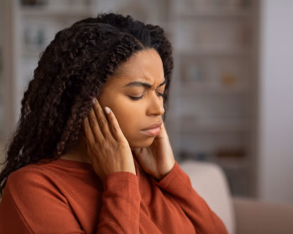 Woman with eyes closed holding her hands to her ears, appearing to experience ear pain or discomfort.