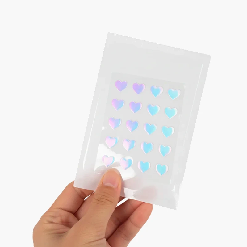 Mano sosteniendo el empaque de Kara Pimple Patch, mostrando la lámina con los parches hidrocoloides en forma de corazón iridiscente