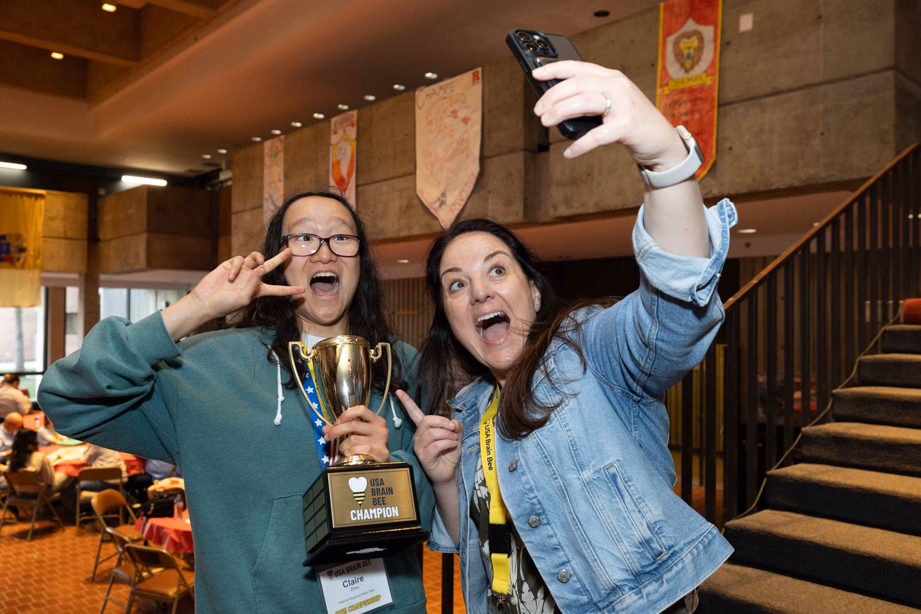 2025 USA Brain Bee champion student holding trophy and celebrating victory with Dr. Manuella Yassa at national competition