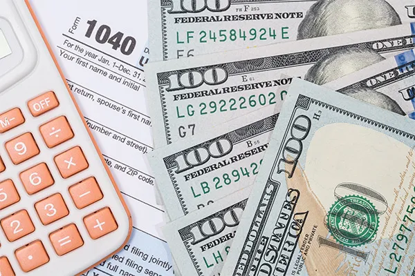 1040 tax form with several hundred dollar bills and calculator