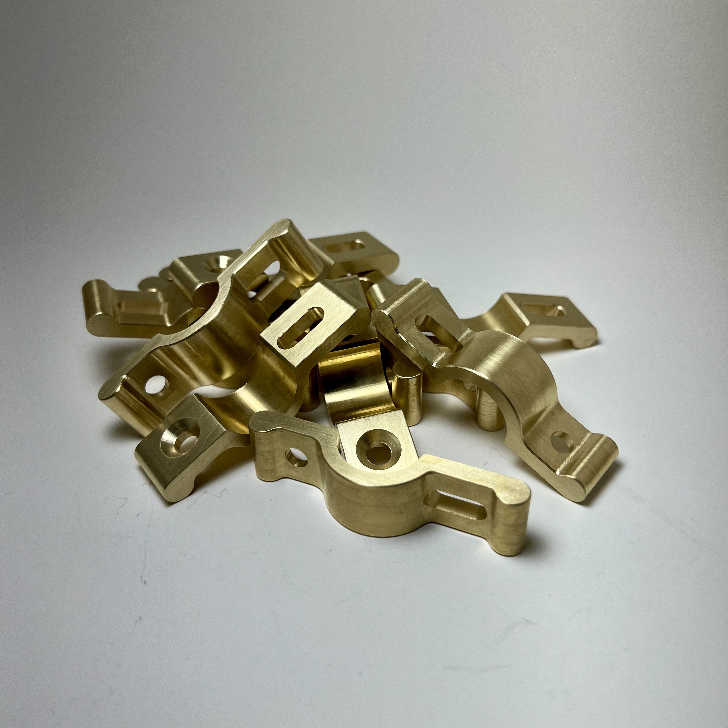Pile of shiny metal brackets with holes on a plain white surface.