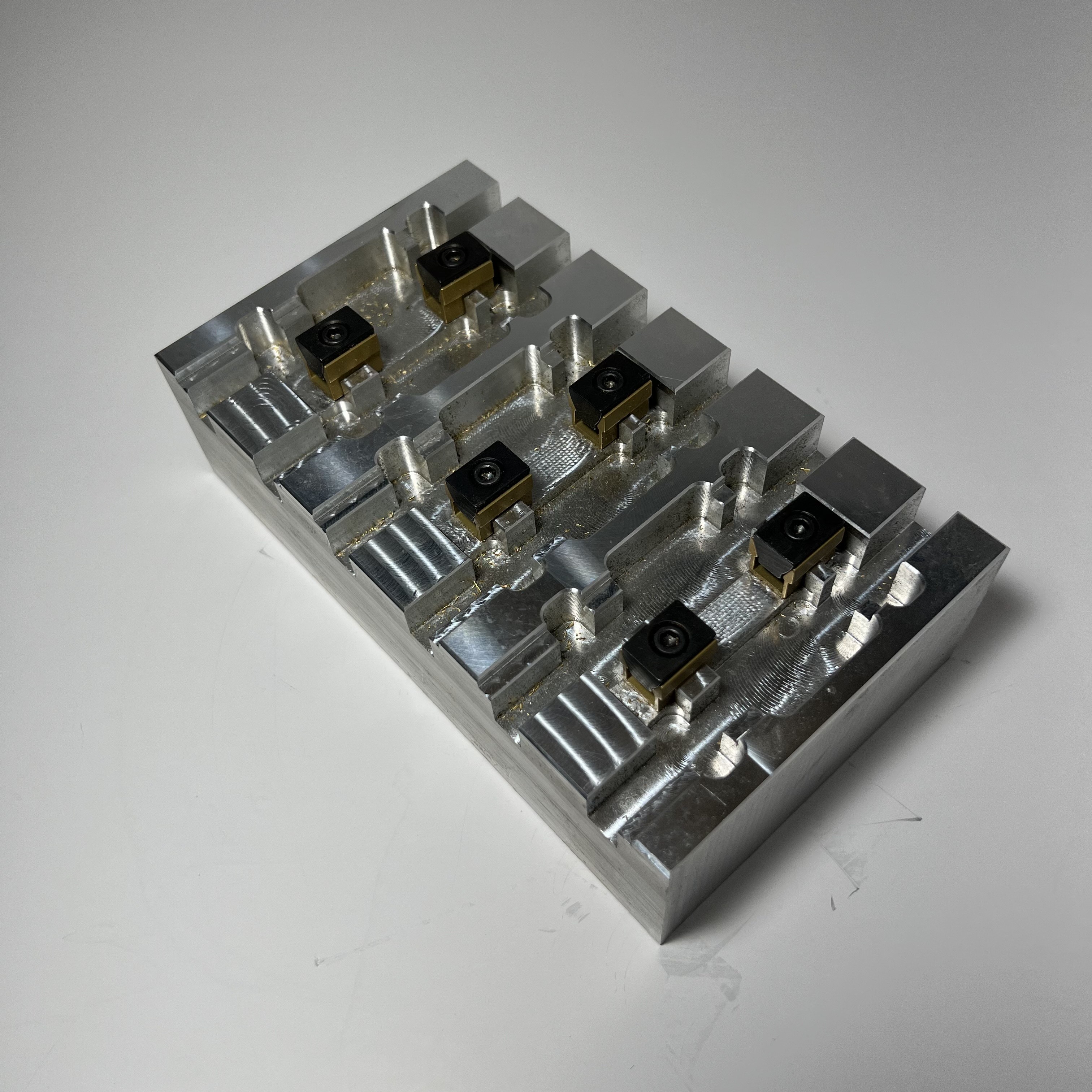 Metal block with four identical compartments, each holding a small black and bronze square component.