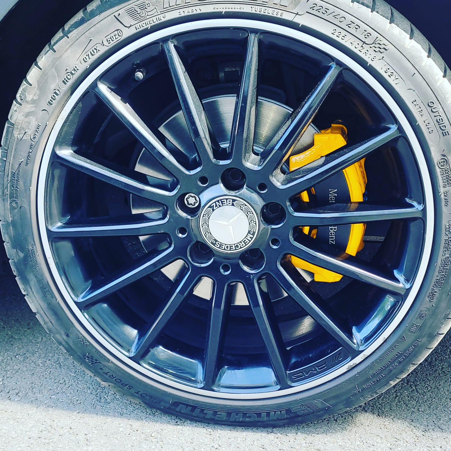 Gros plan d'une jante noire AMG avec logo Mercedes-Benz et étrier de frein jaune sur pneu Michelin.