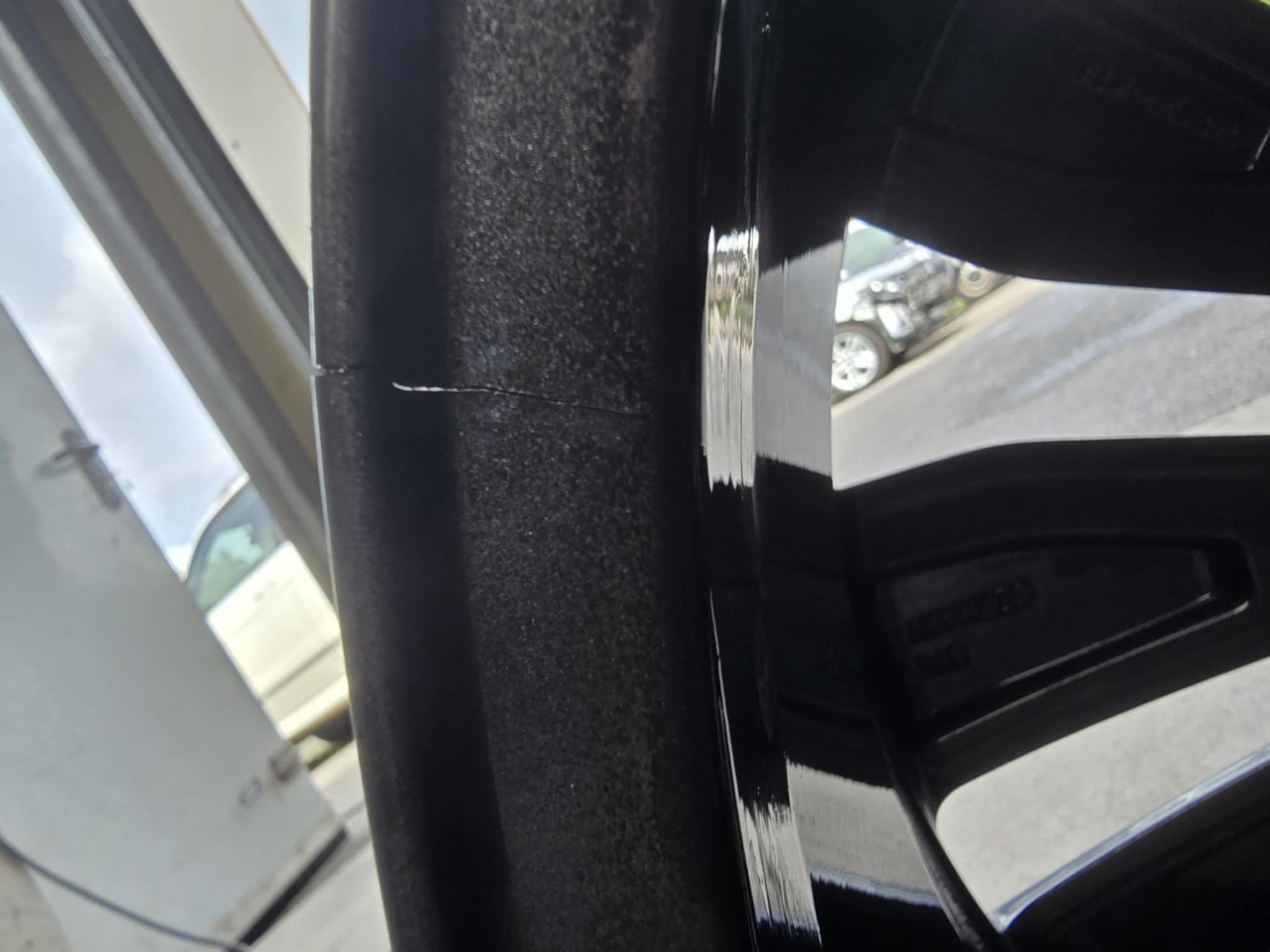Gros plan sur une jante de voiture noire brillante avec une fissure visible sur le bord intérieur.