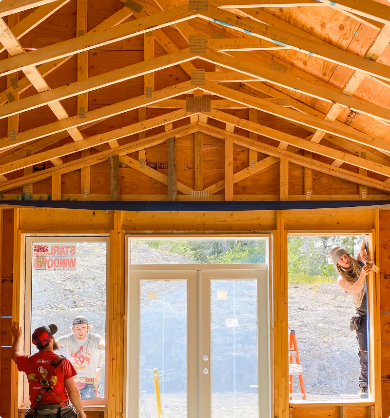 Three construction workers installing windows in a wooden-framed house under construction.