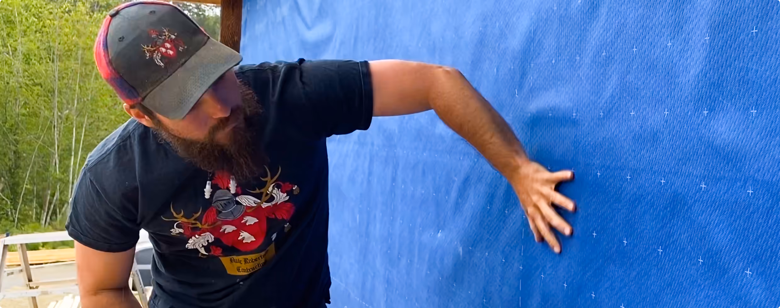 Man with a beard and cap presses his hand against a blue textured surface outdoors.