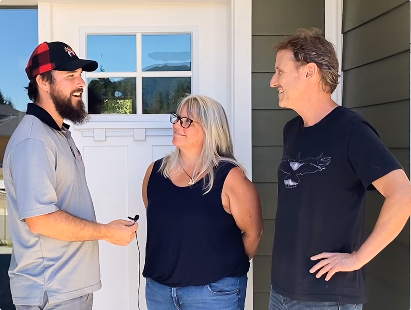 Three people standing outside in front of a white door with window, engaged in conversation and smiling.