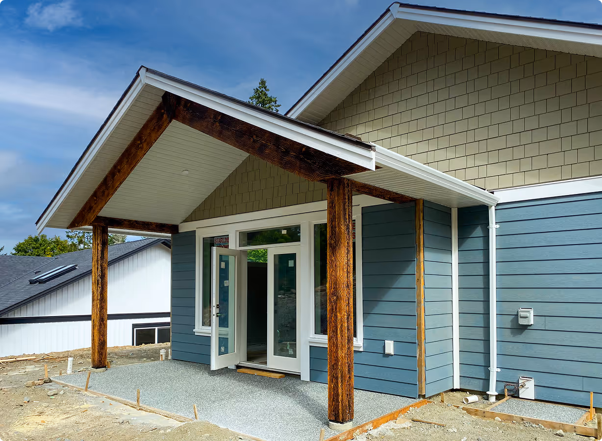 Front porch of a modern house under construction with blue siding, white trim, and stained wooden support beams.
