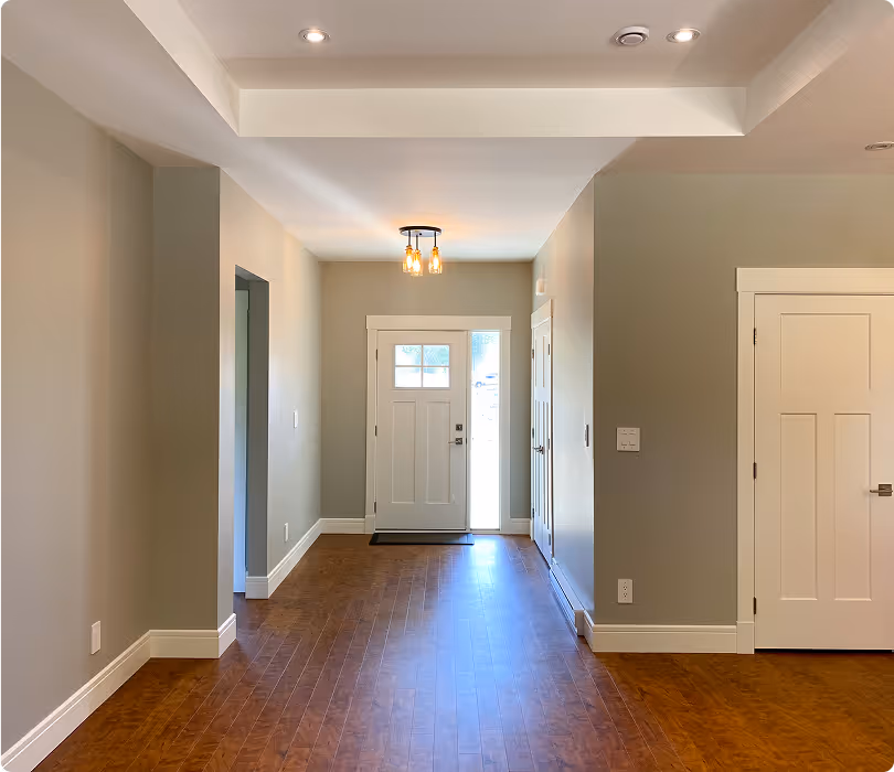 Empty hallway with wooden floor leading to a white front door with windows and an overhead light fixture.