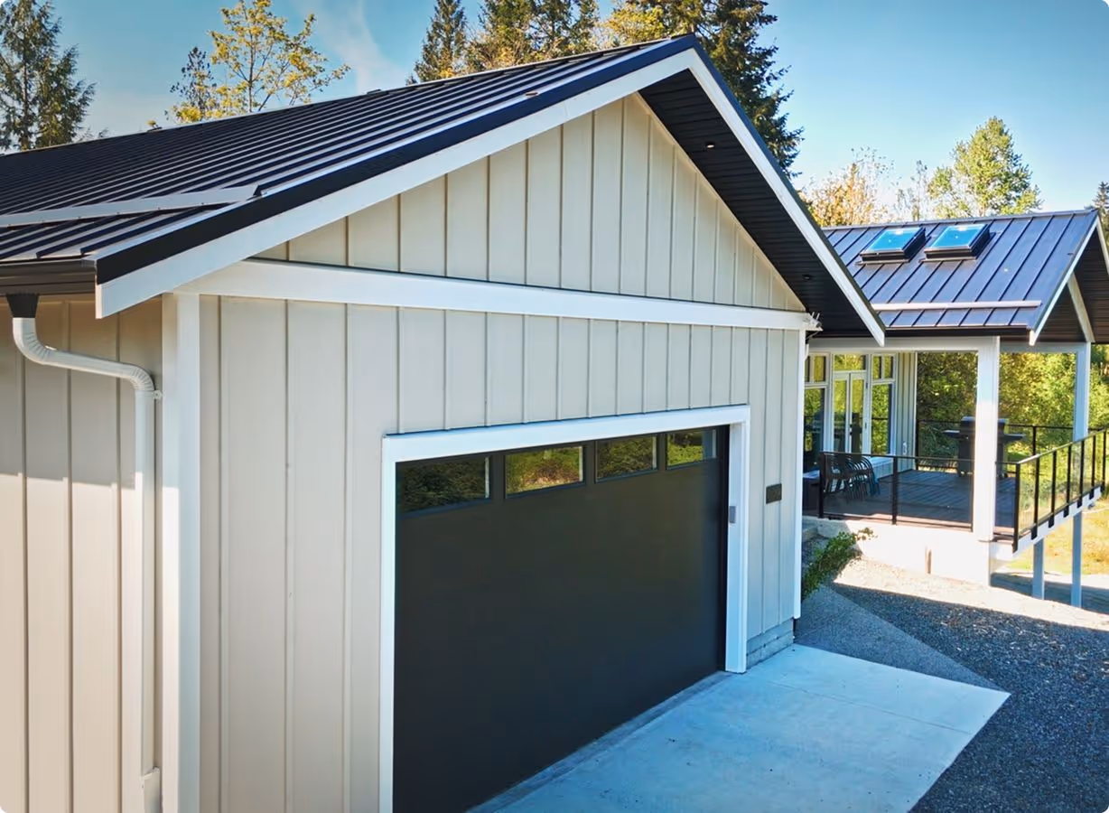 Modern house exterior with beige siding, black metal roof, and a closed black garage door.