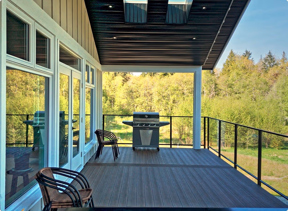 Covered wooden deck with a grill and two stacks of chairs, overlooking a green forested landscape.