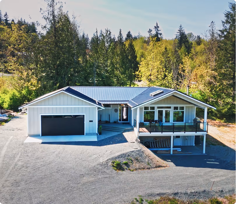 Modern single-story house with attached garage, large windows, and balcony surrounded by dense green trees.