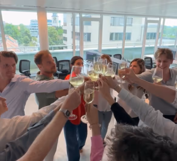 Group of people in an office setting toasting with glasses of white wine.