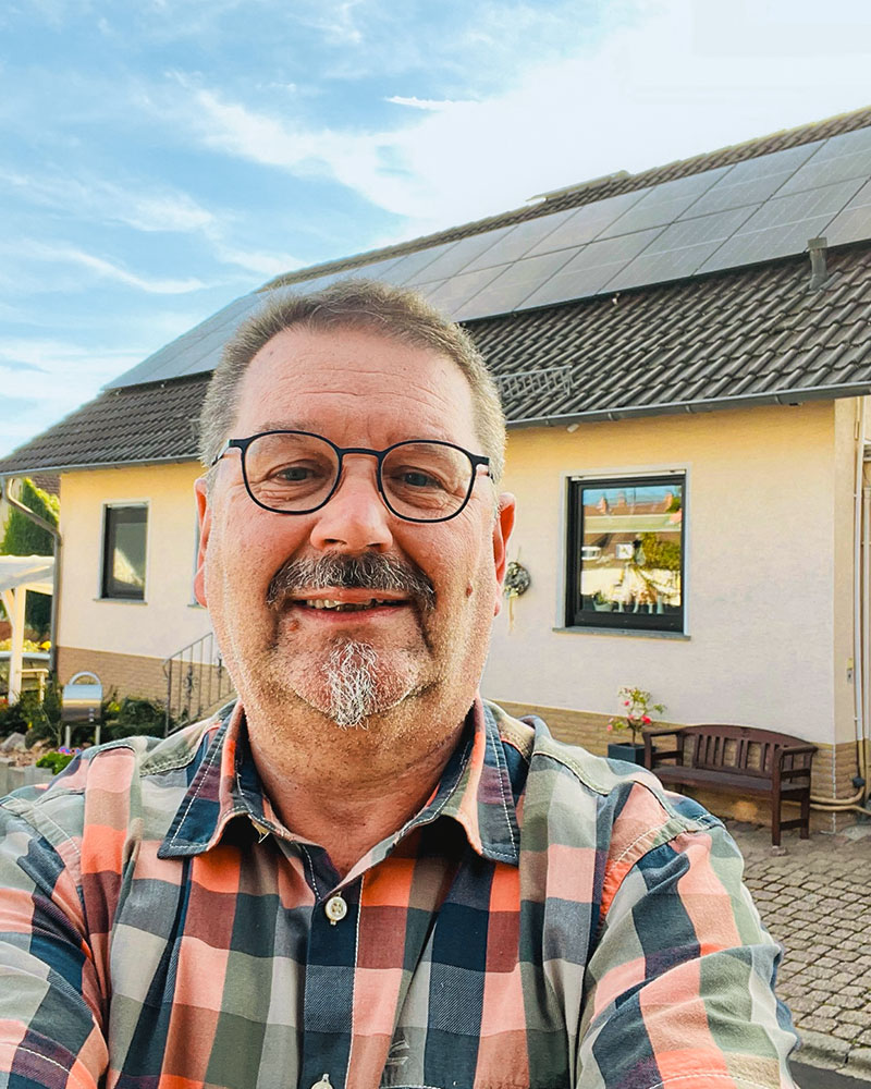 Lächelnder Mann vor Haus mit Solaranlage auf dem Dach