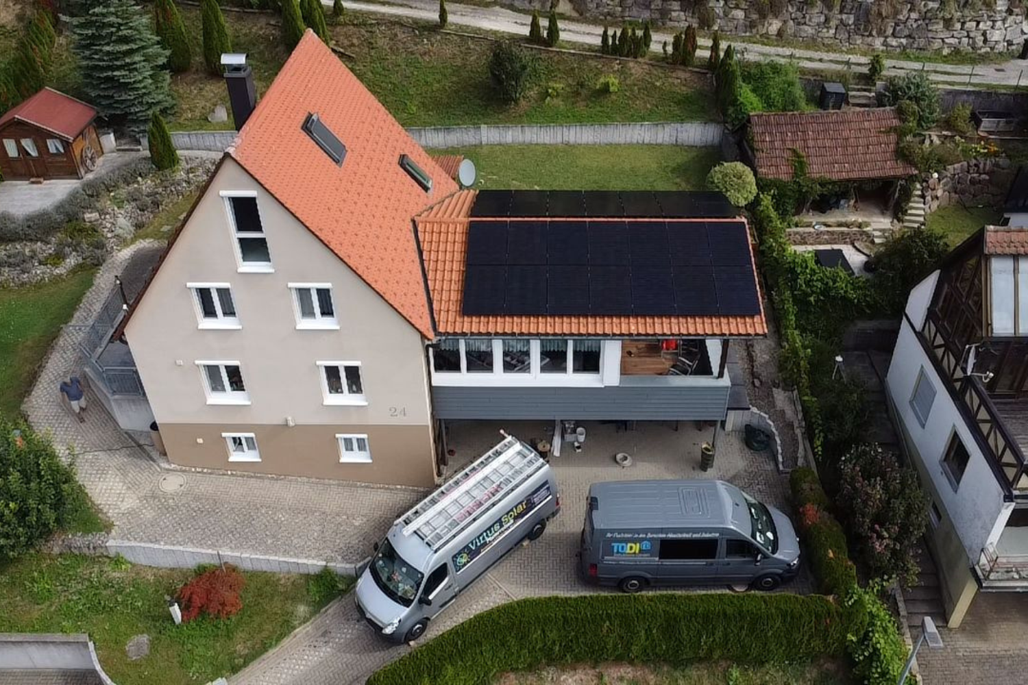 Luftaufnahme eines Hauses mit Solarpanels und zwei Lieferwagen