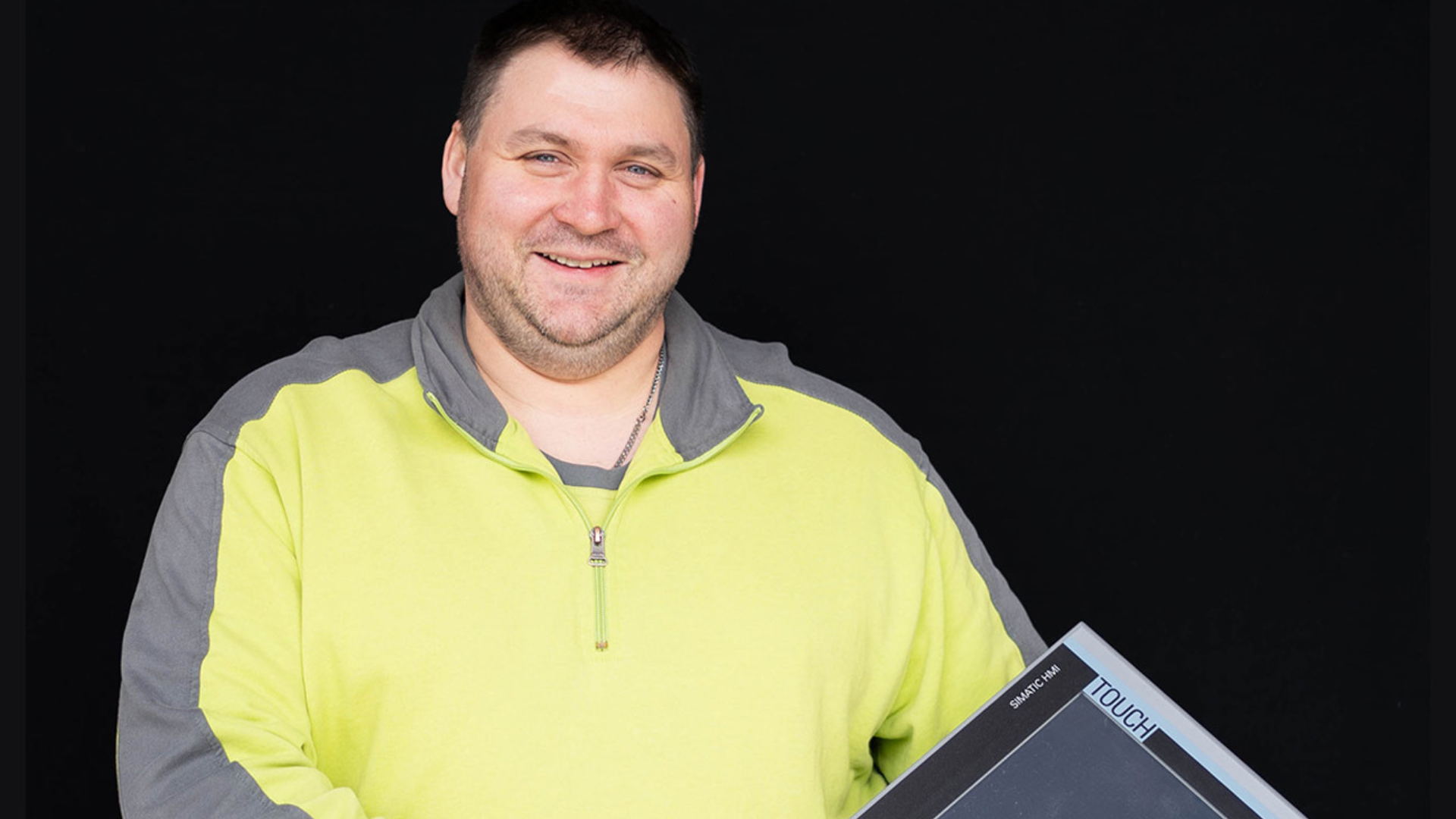 Lächelnder Mann im gelben Pullover mit Touchscreen-Gerät vor schwarzem Hintergrund