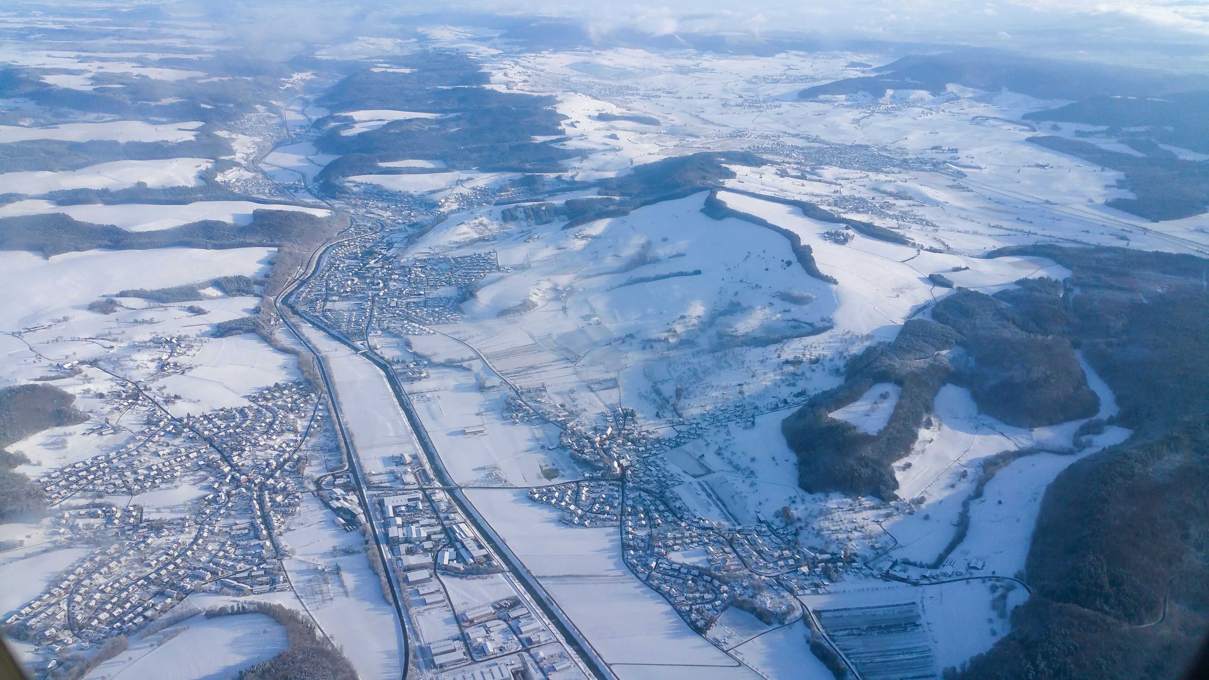 Mit Schnee bedecktes Dach mit Solarzellen an sonnigem Wintertag neben schneebedeckten Tannenbäumen.