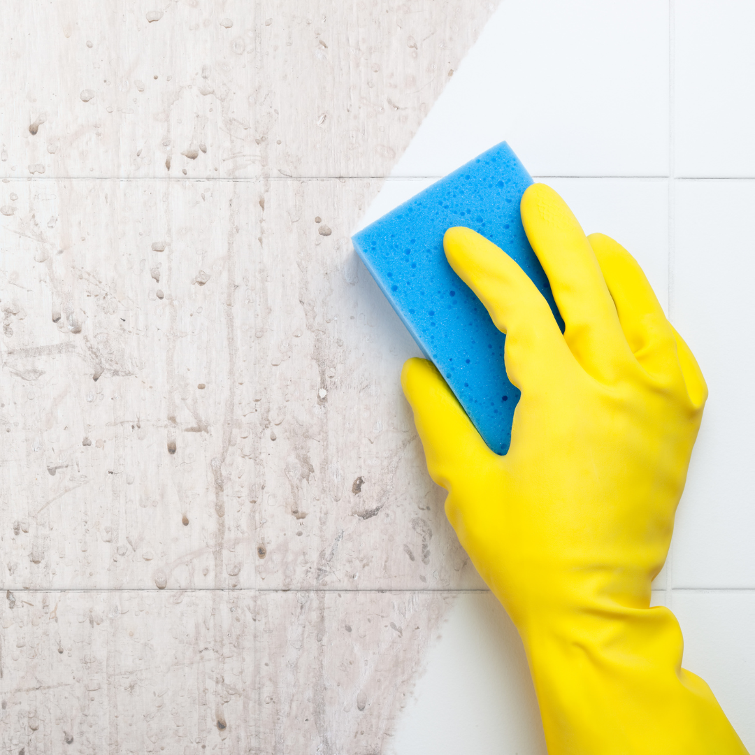 Yellow-gloved hand deep cleaning tile grout with a blue sponge during a short-term rental property refresh.