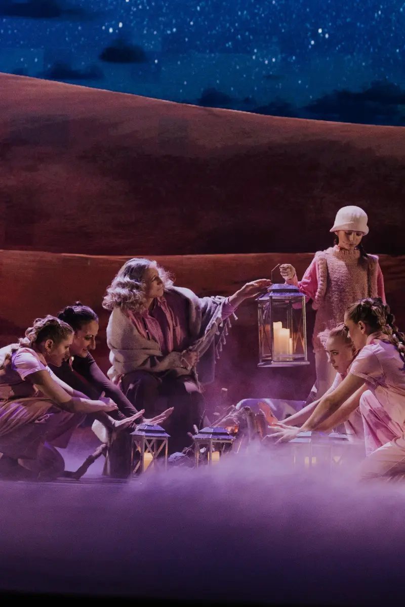 Bühnenbild einer Weihnachtsaufführung mit Tänzern und einer Frau, die Laternen hält