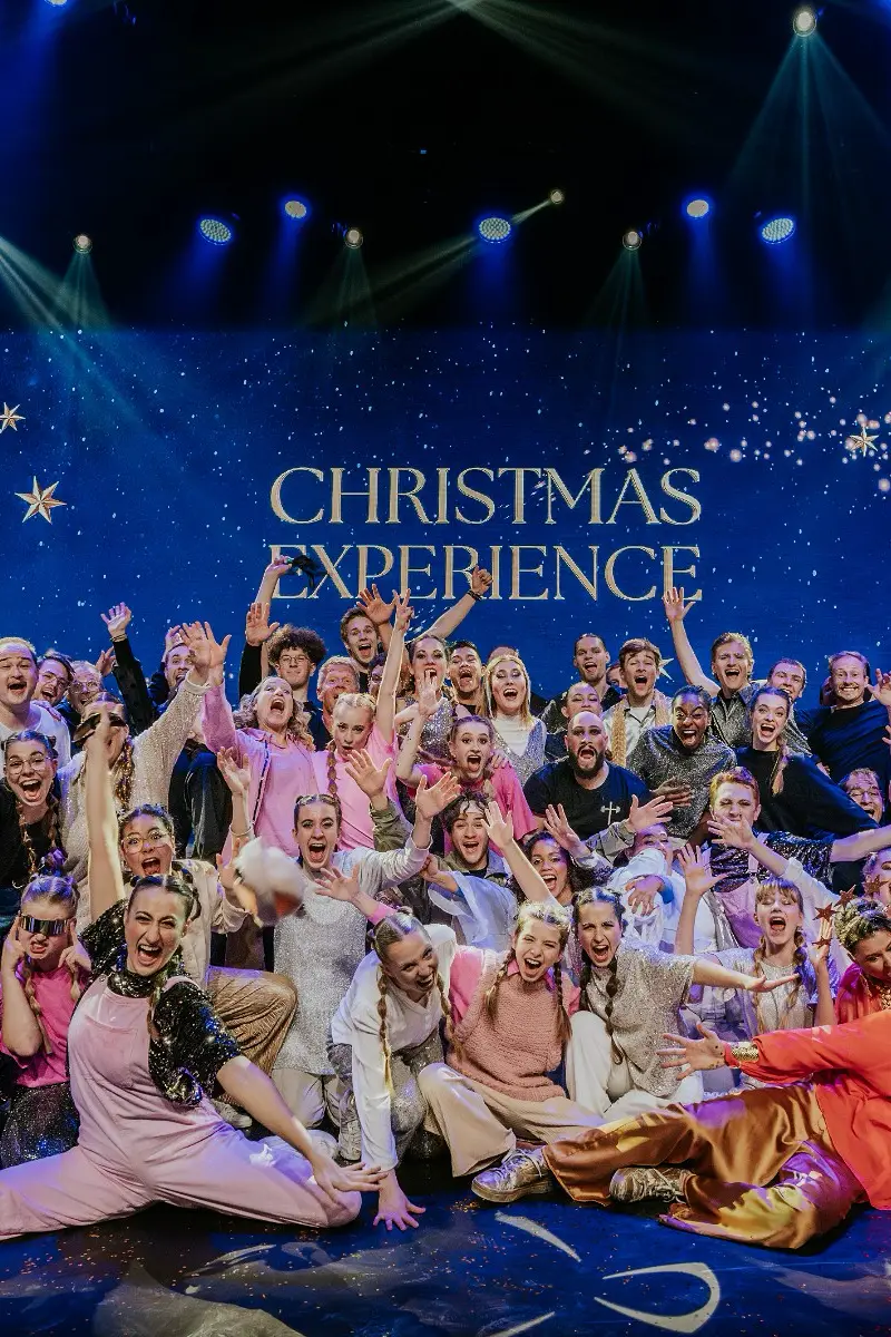 Gruppenfoto der Darsteller des "Christmas Experience"-Events auf der Bühne mit strahlendem Hintergrund