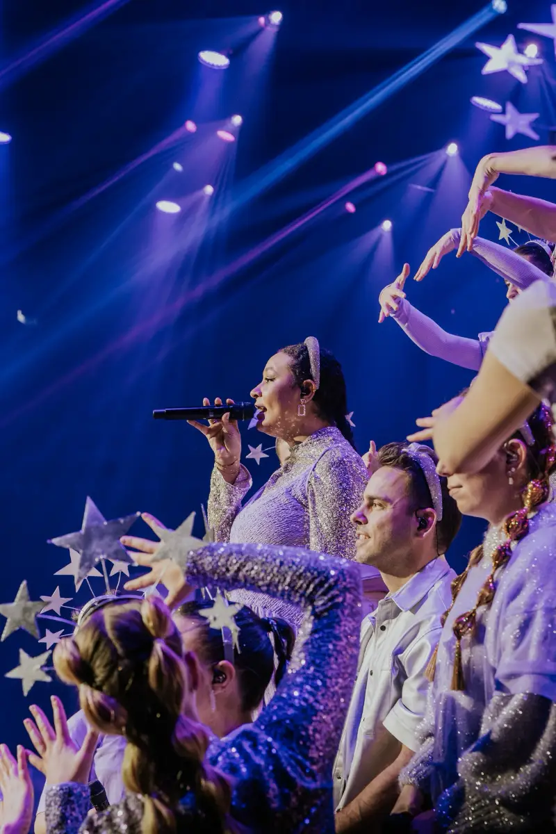 Chor mit funkelnden Kostümen und Sternenkränzen auf der Bühne, Sängerin im Mittelpunkt