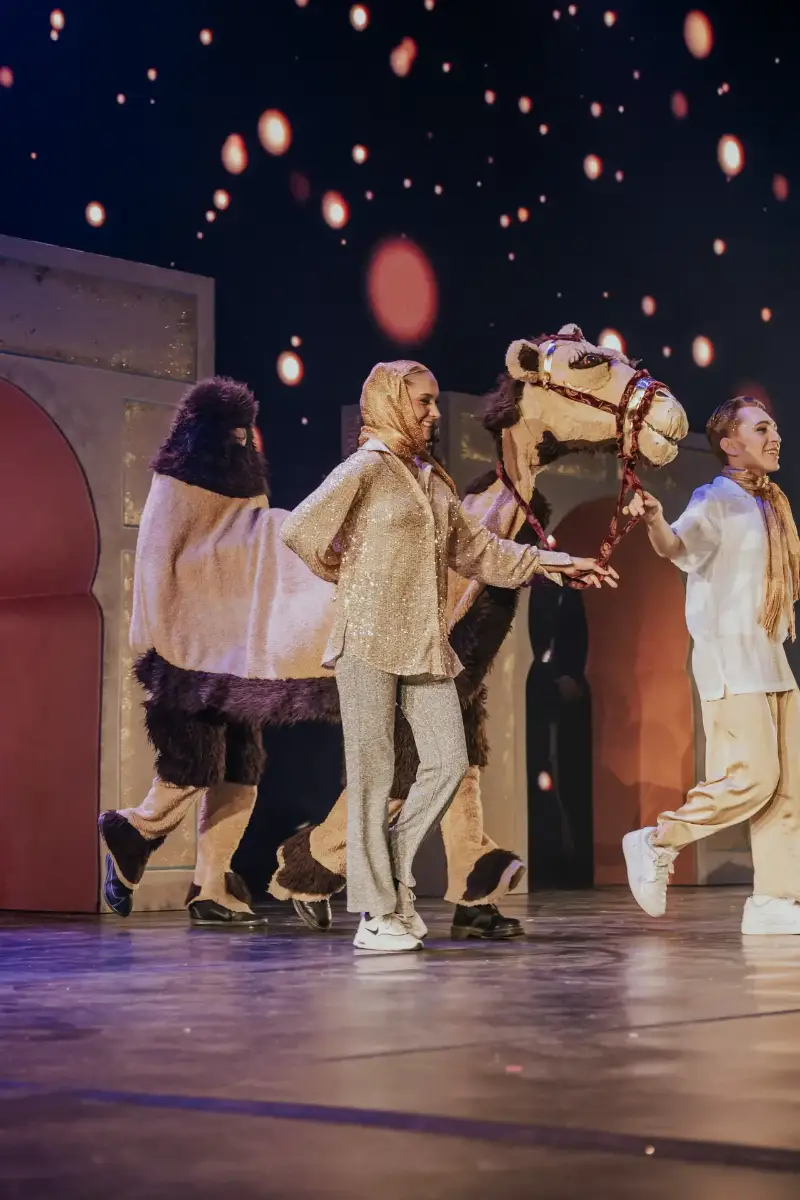 Szenenbild aus der Weihnachtsaufführung mit einem Kameltier und Darstellern auf der Bühne