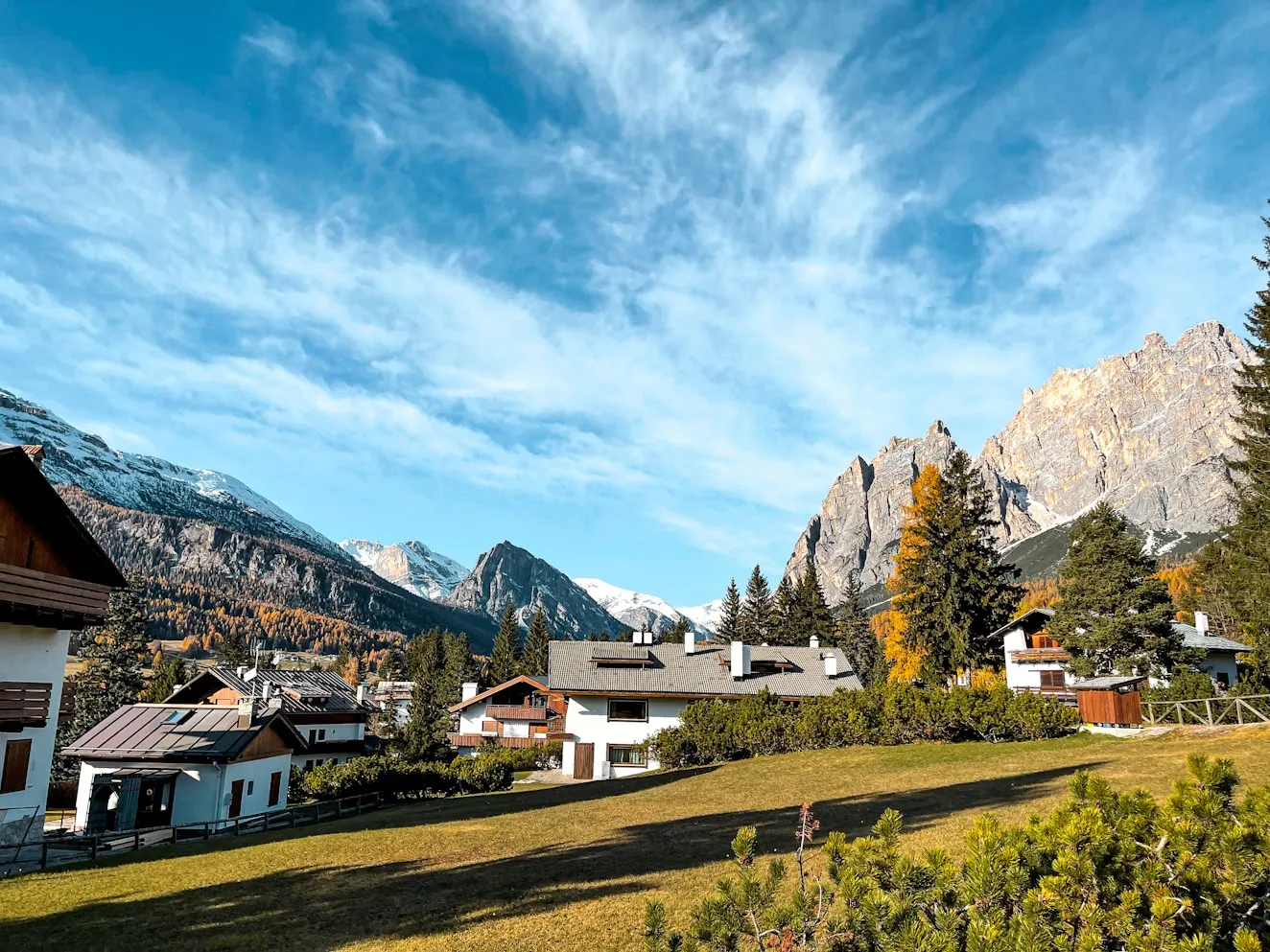 Mountain village with houses and trees under a blue sky.